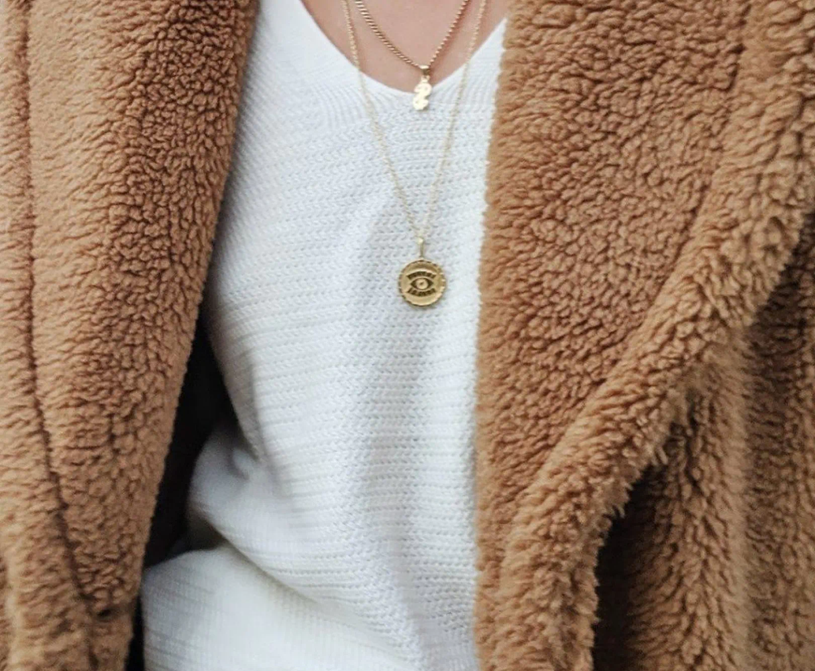 A person in a fleece pullover and white top shows off a gold necklace.