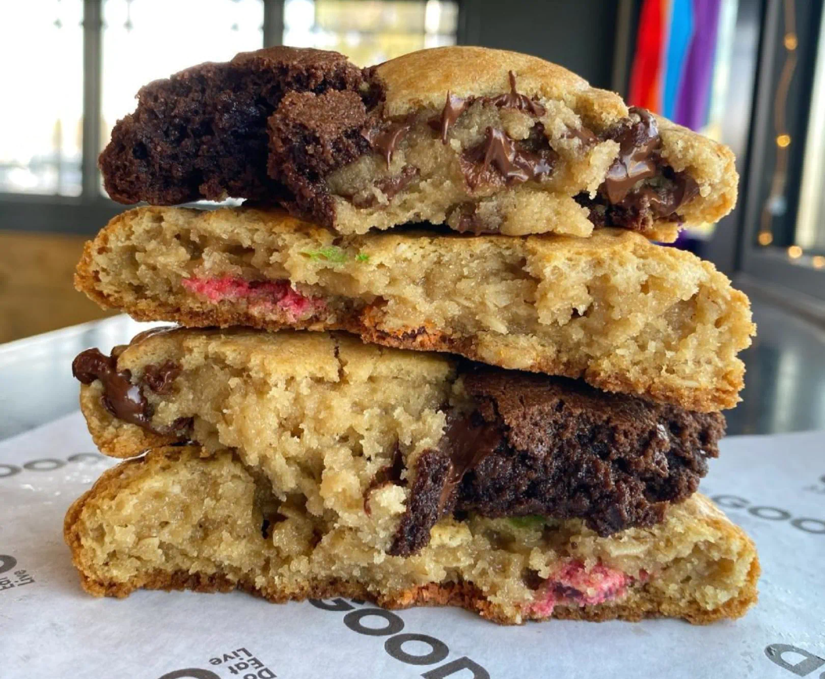 Four large cookies lay stacked on top of one another, full of chocolate and sprinkles.